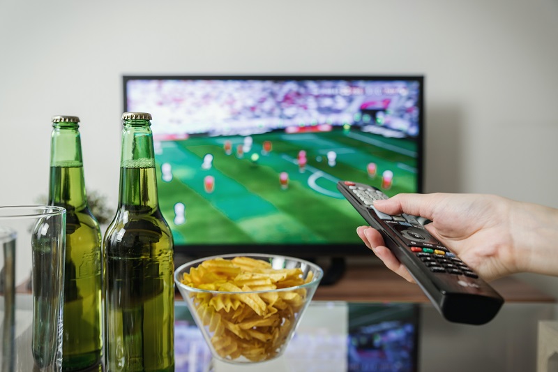 persona viendo deporte en televisión y bebiendo alcohol