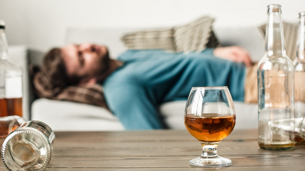 Hombre tumbado en el sofá bajo los efectos del alcohol junto a una botella en el centro de la mesa